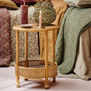 Rundt sidebord i rattan stylet med vase og lys foran farverige t�pper