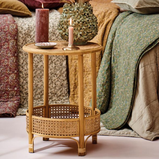Rundt sidebord i rattan stylet med vase og lys foran farverige t�pper