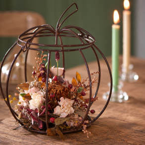 Skulpturelt gr�skar fyldt med t�rrede blomster p� r�t tr�bord