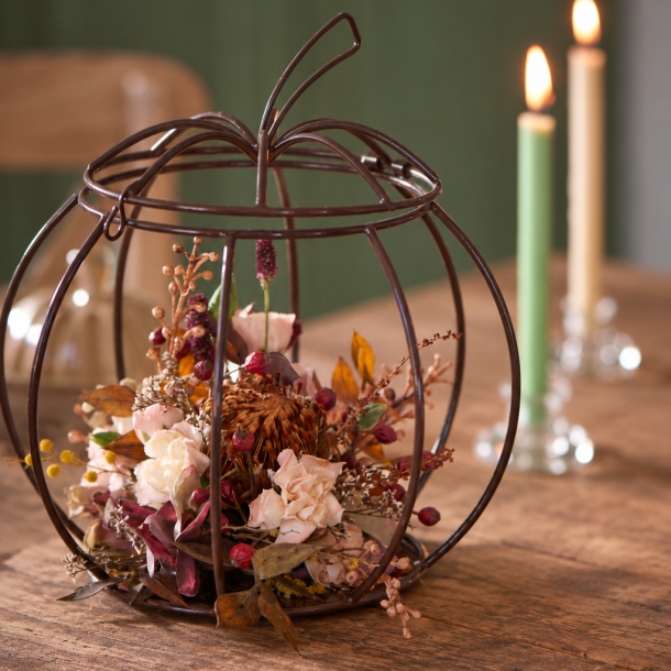 Skulpturelt gr�skar fyldt med t�rrede blomster p� r�t tr�bord