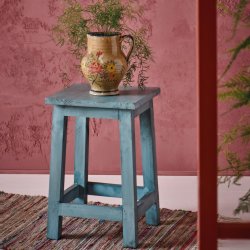Bl� skammel p� v�vet kludet�ppe foran varm rosa v�g med keramikkande og gr�nne grene